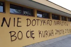 Żółta ściana budynku z odręcznym czarnym napisem ostrzegającym przed narkotykami, zakończonym słowami „zmiotą z planszy”