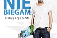 Plakat z napisem „Nie biegam i cieszę się życiem”, obok uśmiechnięty mężczyzna w okularach i białym T-shircie z deskorolką w ręku